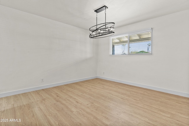 empty room featuring a notable chandelier, wood finished floors, and baseboards