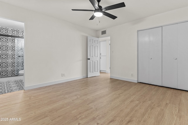unfurnished bedroom with visible vents, baseboards, wood finished floors, a closet, and ensuite bath
