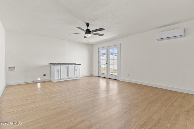 spare room with baseboards, a wall mounted air conditioner, light wood-style floors, a textured ceiling, and a ceiling fan