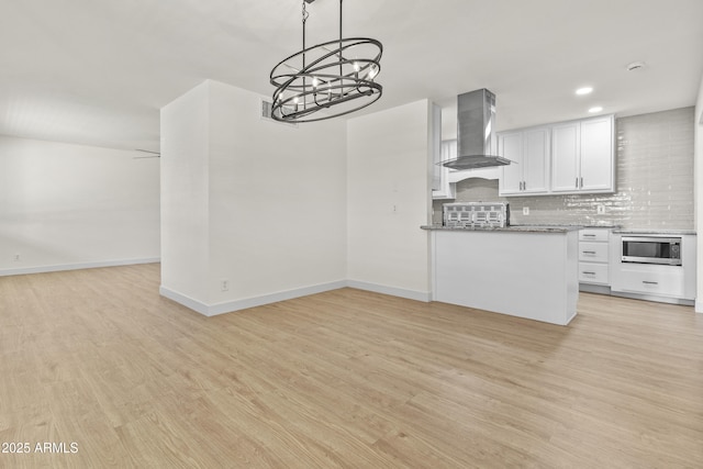 kitchen with stainless steel microwave, tasteful backsplash, wall chimney exhaust hood, and light wood-style flooring