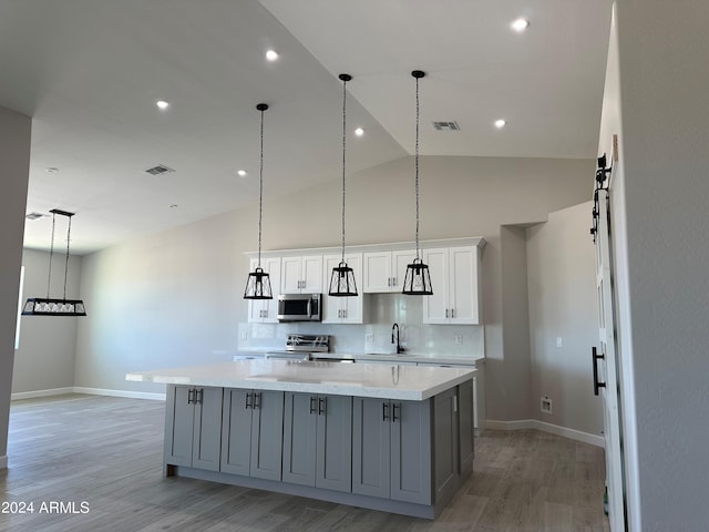 kitchen with appliances with stainless steel finishes, tasteful backsplash, gray cabinetry, a large island with sink, and white cabinetry