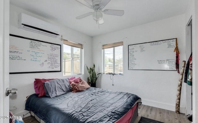 bedroom featuring an AC wall unit, baseboards, ceiling fan, and wood finished floors