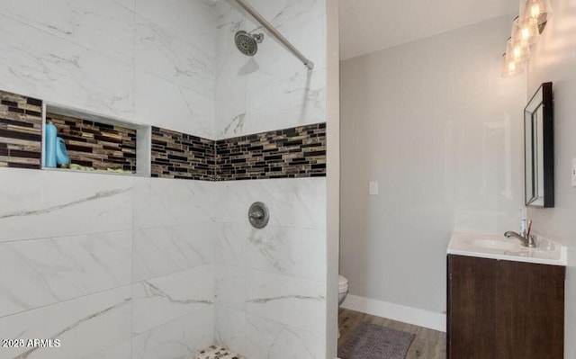 bathroom with a tile shower, wood finished floors, toilet, and vanity