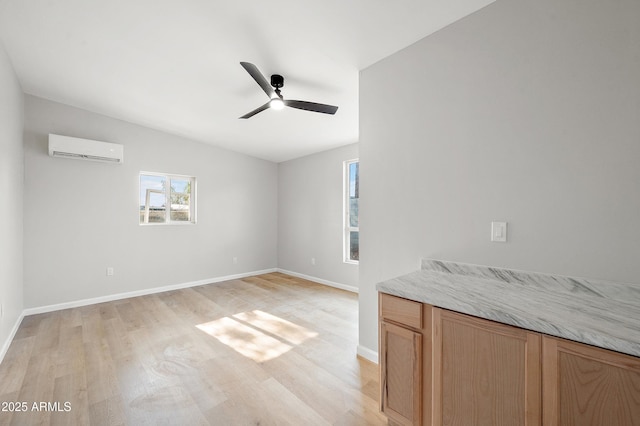 interior space with a wall unit AC, vaulted ceiling, baseboards, ceiling fan, and light wood-style flooring