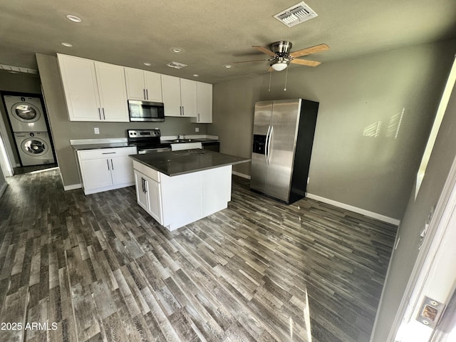 kitchen with stainless steel appliances, visible vents, white cabinets, stacked washing maching and dryer, and dark countertops