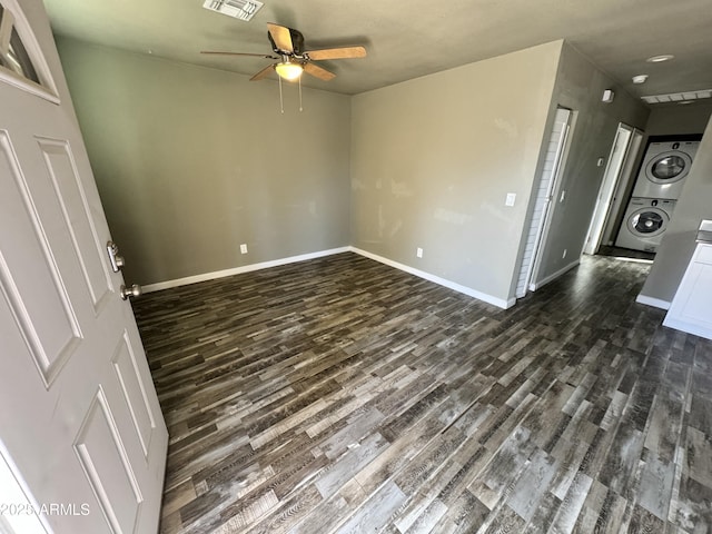 empty room featuring visible vents, dark wood finished floors, stacked washer and clothes dryer, and baseboards