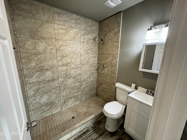 bathroom featuring visible vents, toilet, a tile shower, vanity, and wood finished floors