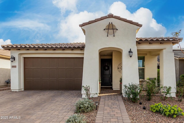 mediterranean / spanish home featuring a garage, decorative driveway, a tile roof, and stucco siding