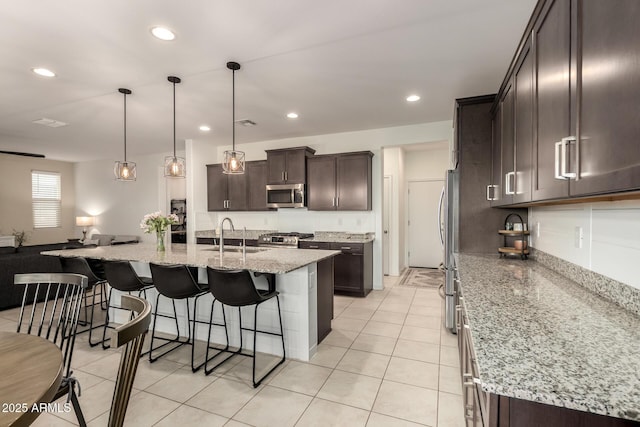 kitchen with dark brown cabinetry, recessed lighting, stainless steel appliances, a sink, and a kitchen breakfast bar