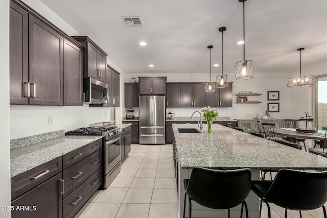 kitchen with visible vents, light stone counters, appliances with stainless steel finishes, dark brown cabinets, and a sink