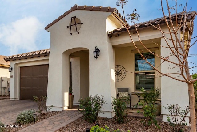 doorway to property featuring a garage, decorative driveway, a tile roof, and stucco siding