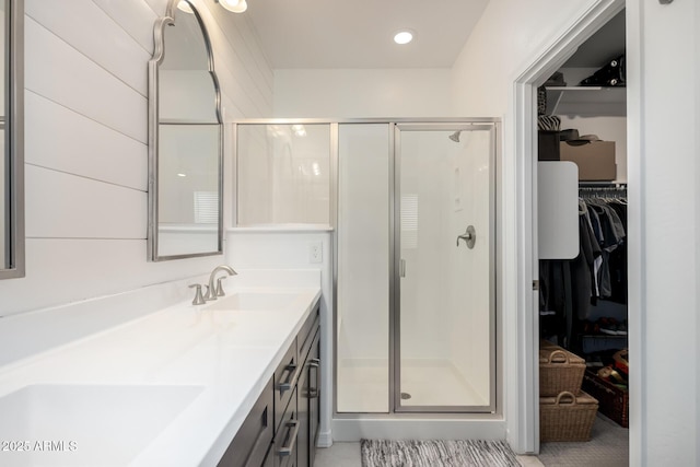 full bathroom featuring double vanity, a shower stall, a walk in closet, and a sink