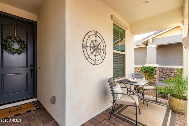 property entrance with stone siding, covered porch, and stucco siding