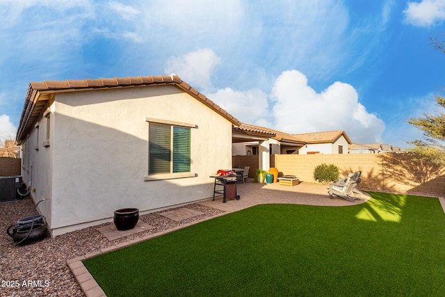 rear view of house featuring a tile roof, a yard, stucco siding, a patio area, and a fenced backyard