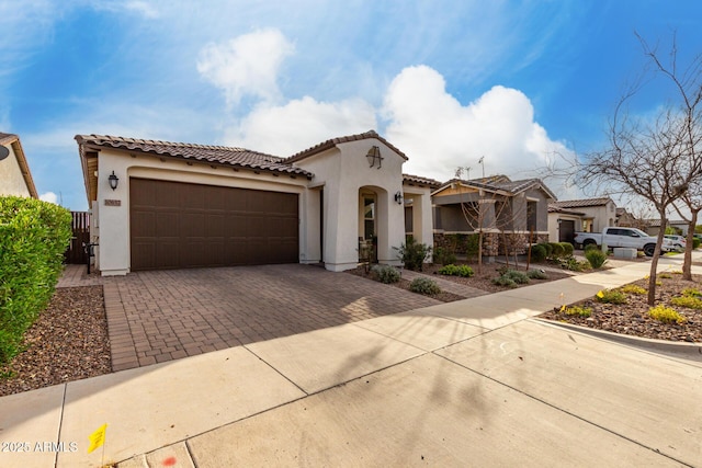 mediterranean / spanish-style home featuring a tiled roof, decorative driveway, an attached garage, and stucco siding