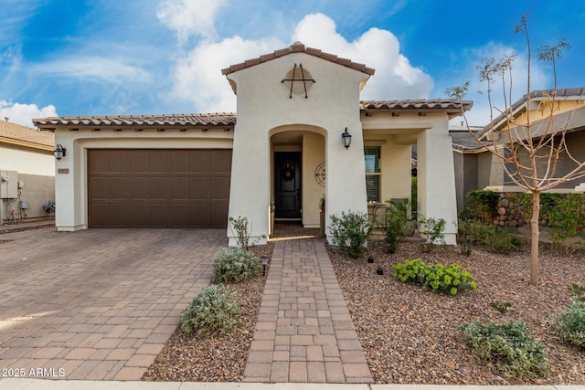 mediterranean / spanish-style home with a garage, a tiled roof, decorative driveway, and stucco siding