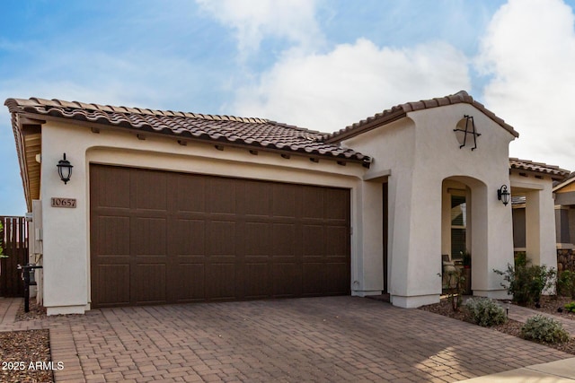 mediterranean / spanish-style house featuring decorative driveway, a tiled roof, an attached garage, and stucco siding