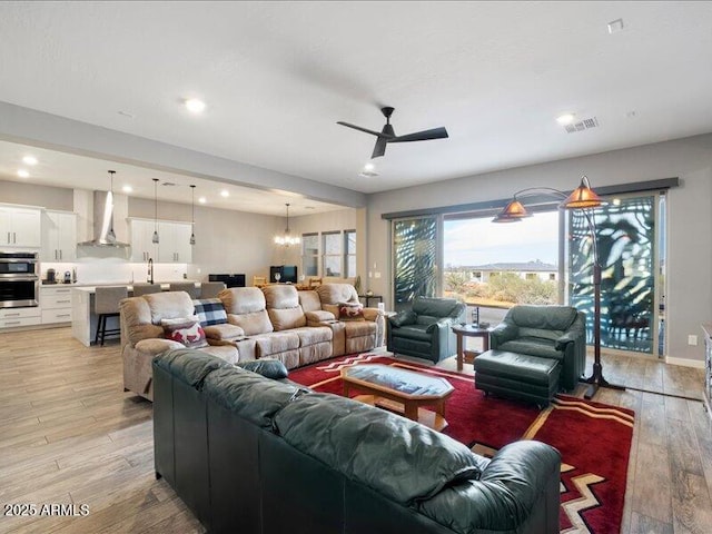 living room with ceiling fan with notable chandelier and light hardwood / wood-style floors