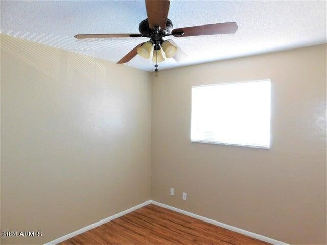 empty room with ceiling fan, wood-type flooring, and a textured ceiling