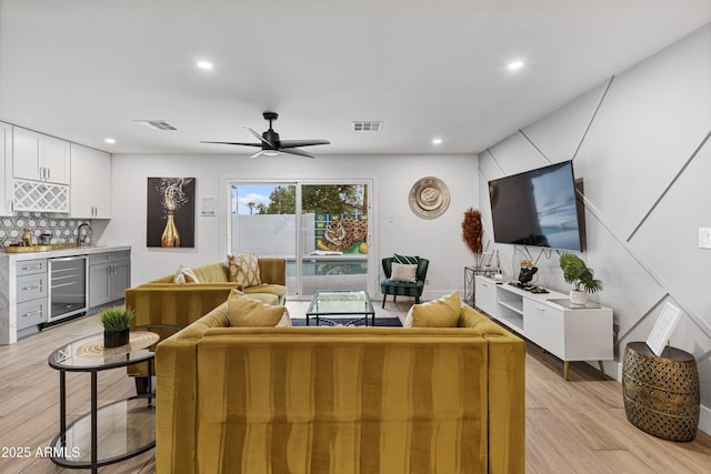 living area featuring light wood finished floors, visible vents, a ceiling fan, indoor wet bar, and beverage cooler