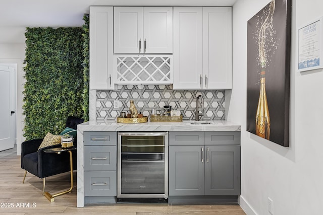 bar with a sink, light wood-type flooring, bar, backsplash, and wine cooler