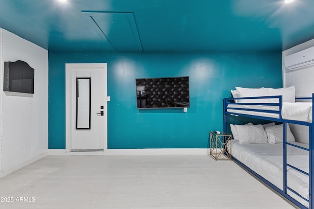 bedroom with wood finished floors, elevator, baseboards, attic access, and a wall mounted AC