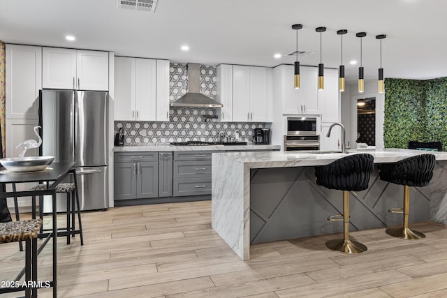 kitchen with wall chimney range hood, decorative backsplash, appliances with stainless steel finishes, gray cabinetry, and visible vents
