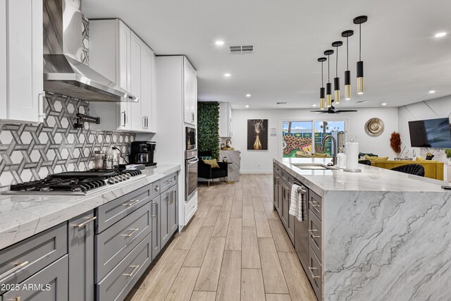 kitchen with stainless steel appliances, visible vents, wall chimney range hood, a sink, and light wood-style flooring