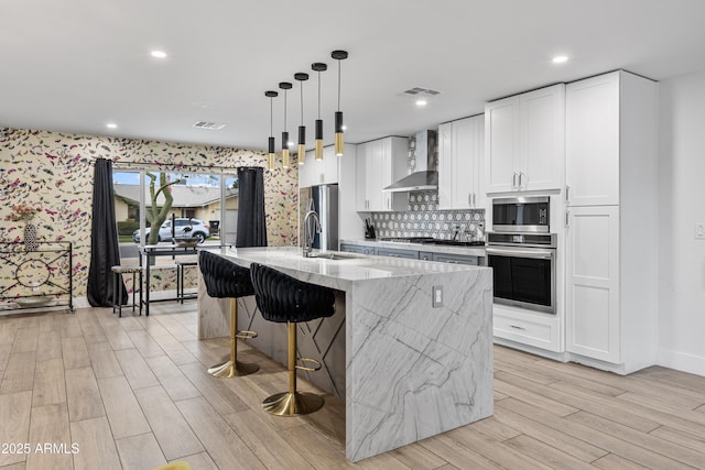 kitchen featuring wall chimney exhaust hood, stainless steel appliances, a sink, visible vents, and wallpapered walls