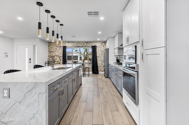 kitchen featuring light wood finished floors, stainless steel appliances, a large island, visible vents, and a sink