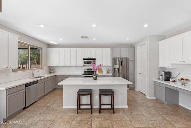 kitchen with tasteful backsplash, gray cabinets, appliances with stainless steel finishes, a sink, and a kitchen island