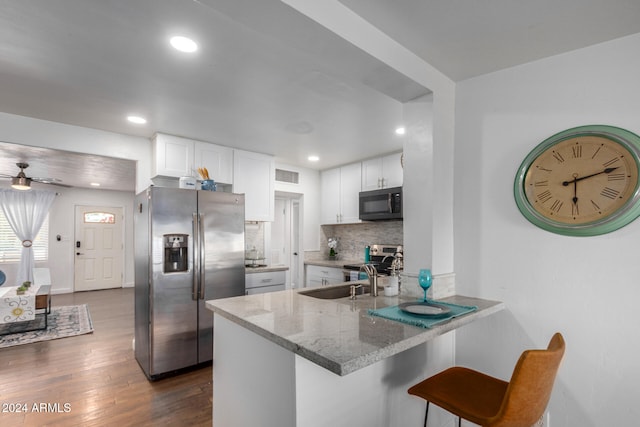 kitchen with white cabinetry, kitchen peninsula, appliances with stainless steel finishes, a kitchen bar, and dark hardwood / wood-style flooring