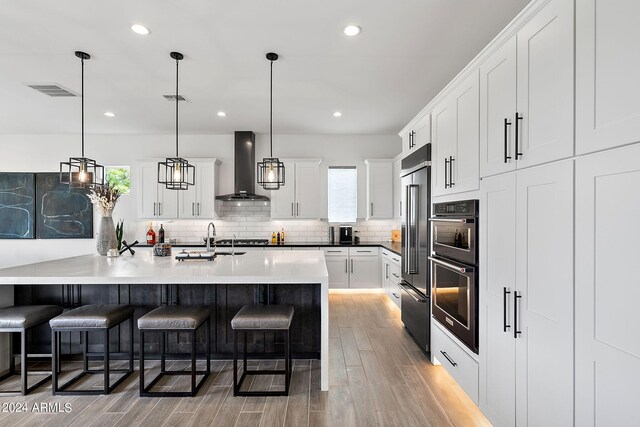 kitchen with white cabinets, light hardwood / wood-style flooring, pendant lighting, backsplash, and wall chimney range hood