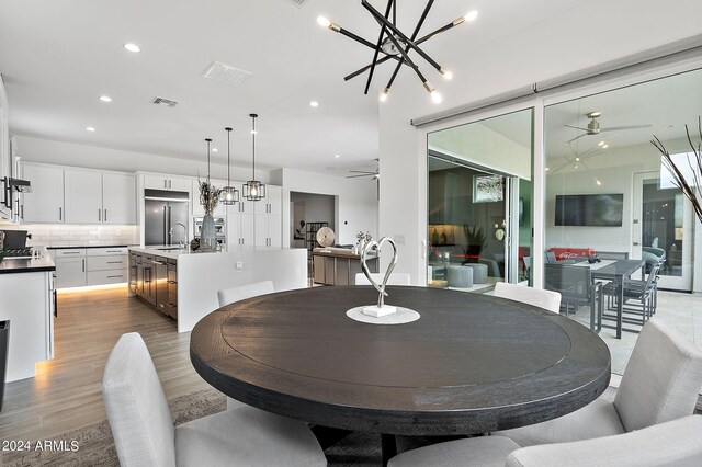 dining space featuring light hardwood / wood-style floors, sink, and ceiling fan with notable chandelier