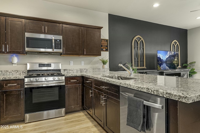 kitchen featuring sink, light hardwood / wood-style floors, kitchen peninsula, stainless steel appliances, and light stone countertops