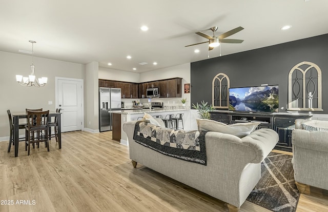 living room featuring ceiling fan with notable chandelier and light hardwood / wood-style floors