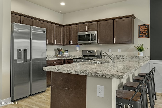 kitchen with light hardwood / wood-style floors, stainless steel appliances, a breakfast bar, and kitchen peninsula