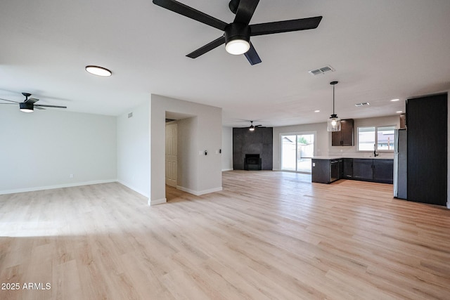 unfurnished living room with ceiling fan, a fireplace, sink, and light hardwood / wood-style floors