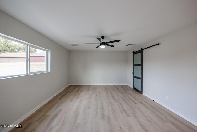 unfurnished room featuring ceiling fan, light hardwood / wood-style flooring, and a barn door