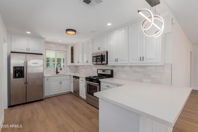 kitchen featuring decorative light fixtures, white cabinetry, sink, kitchen peninsula, and stainless steel appliances