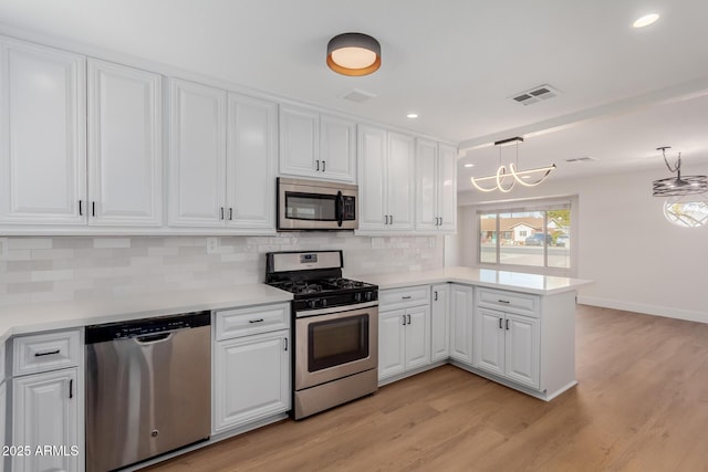 kitchen with appliances with stainless steel finishes, decorative light fixtures, white cabinets, and kitchen peninsula