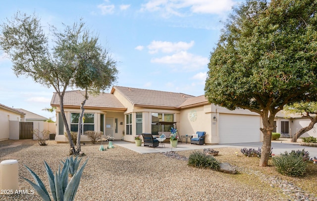 view of front of house with fence, a tile roof, stucco siding, driveway, and an attached garage