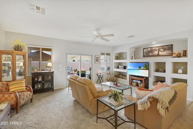 living area with built in shelves, light colored carpet, visible vents, and ceiling fan