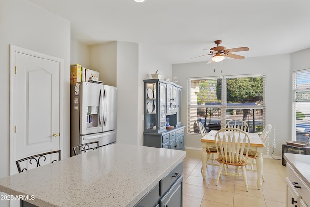 kitchen with gray cabinetry, light stone counters, stainless steel fridge, light tile patterned floors, and ceiling fan