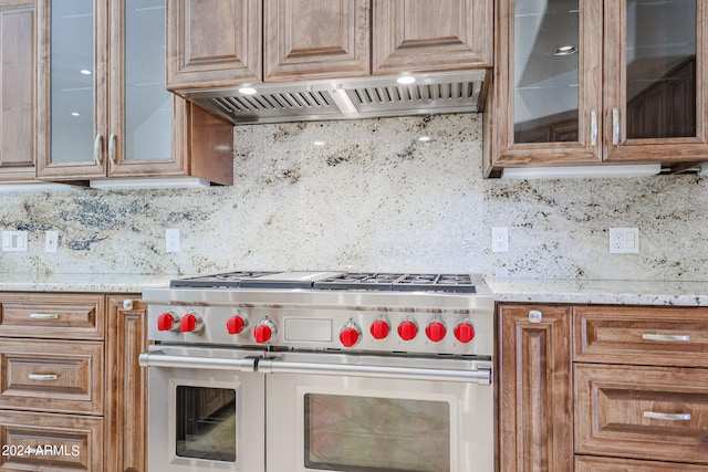 kitchen featuring range with two ovens, light stone counters, ventilation hood, and decorative backsplash