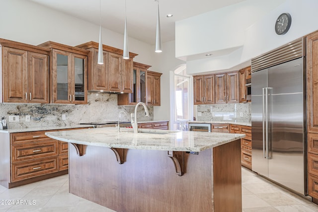 kitchen with a center island with sink, light stone countertops, tasteful backsplash, and built in refrigerator