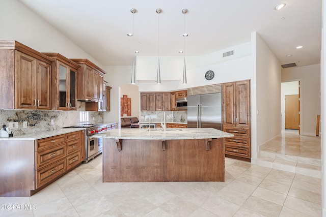 kitchen featuring high end appliances, light stone countertops, a breakfast bar area, decorative backsplash, and a kitchen island with sink