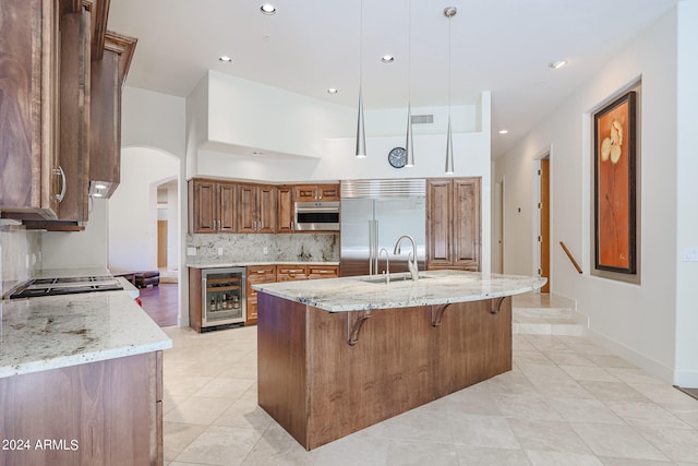 kitchen with backsplash, hanging light fixtures, light stone countertops, stainless steel appliances, and beverage cooler