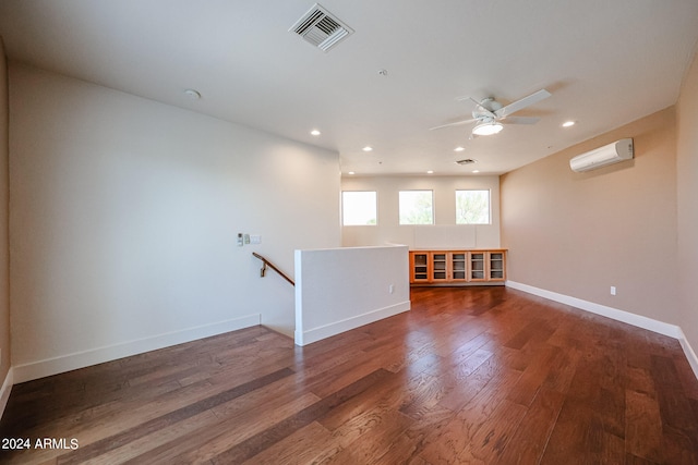 spare room with a wall mounted AC, dark wood-type flooring, and ceiling fan