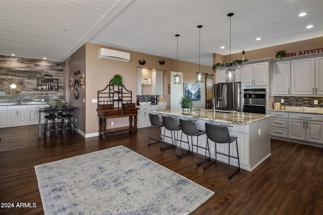 kitchen featuring stainless steel appliances, a spacious island, pendant lighting, an AC wall unit, and white cabinetry